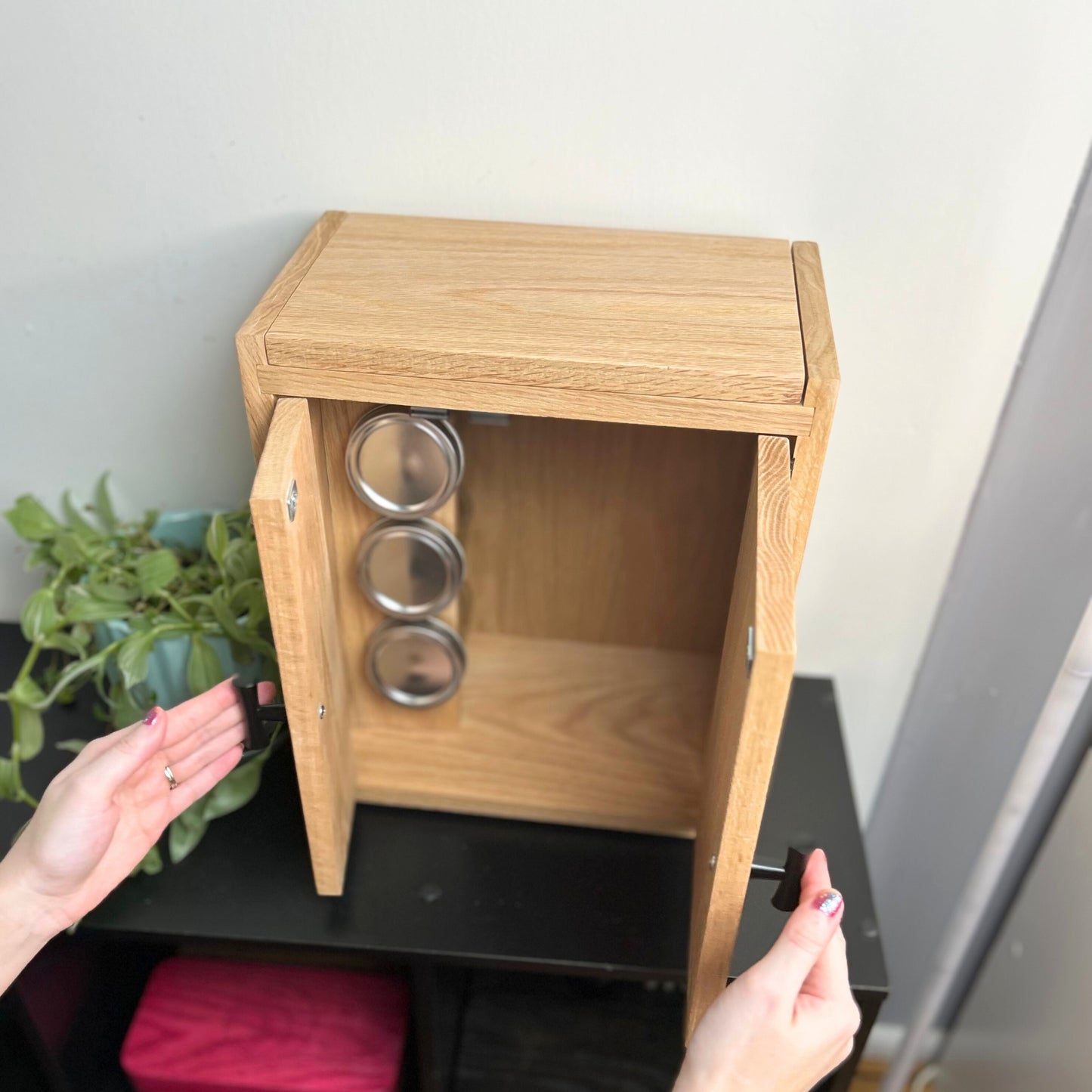 Oak storage cabinet with top hidden compartment for accessories and main section for neatly arranged jars.