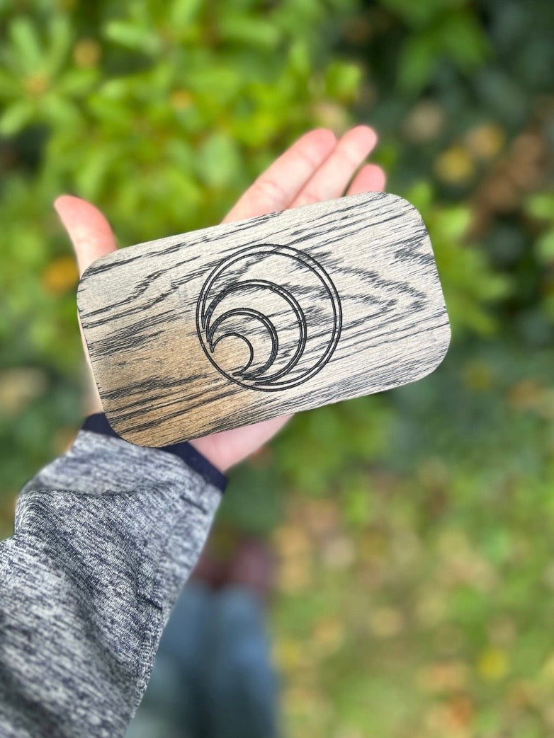 Hand holding a wooden herb case with a spiral design against a blurred green background