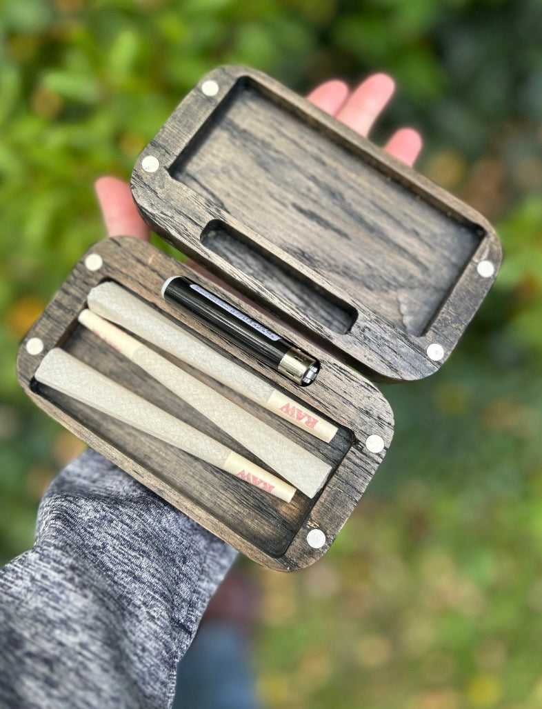 Wooden case with prerolls held by a person against a blurred green background