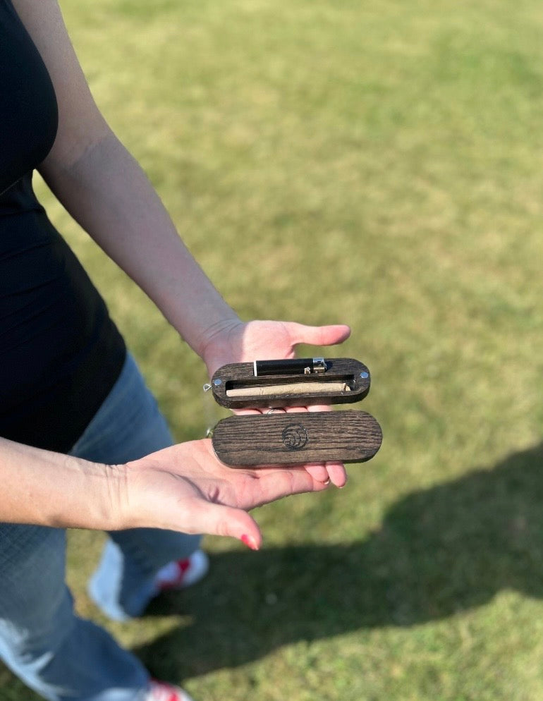 Person holding a wooden lighter case with a metal component against a grassy background