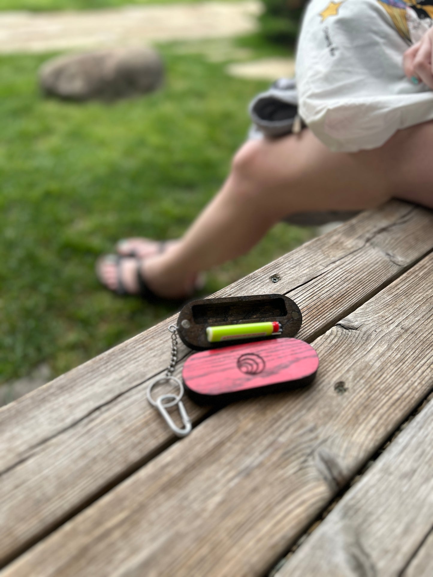 Red Keychain small cases on a wooden surface with a blurred background of grass and legs.