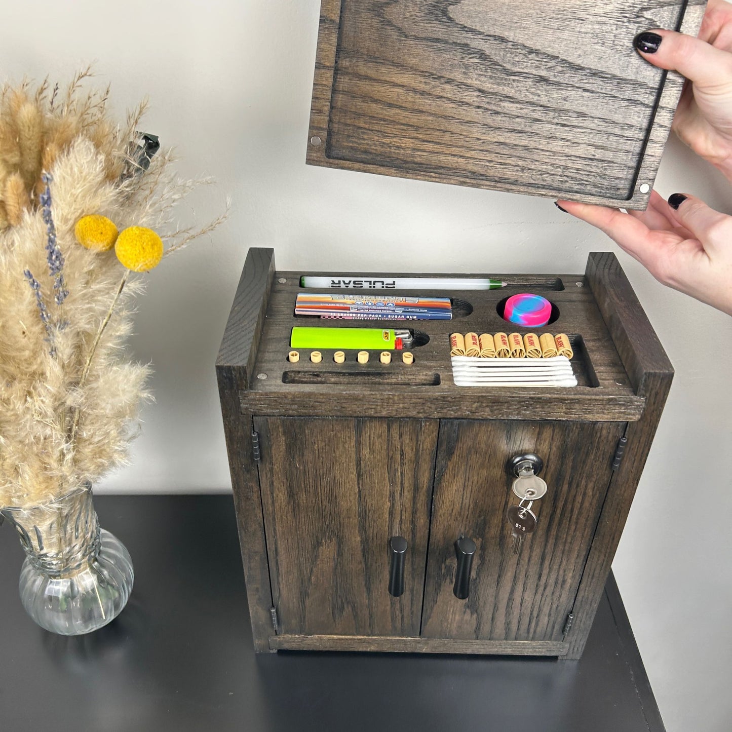 Wooden stash box with compartments on a table next to a vase with dried flowers.