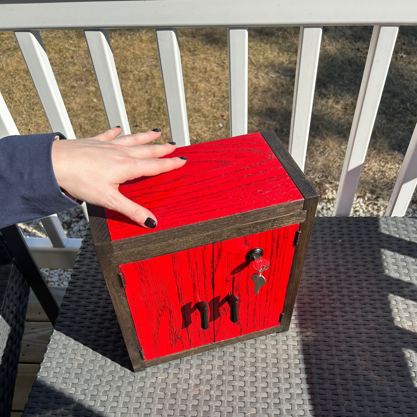 Red wooden stash box with a handle on a wicker chair outdoors