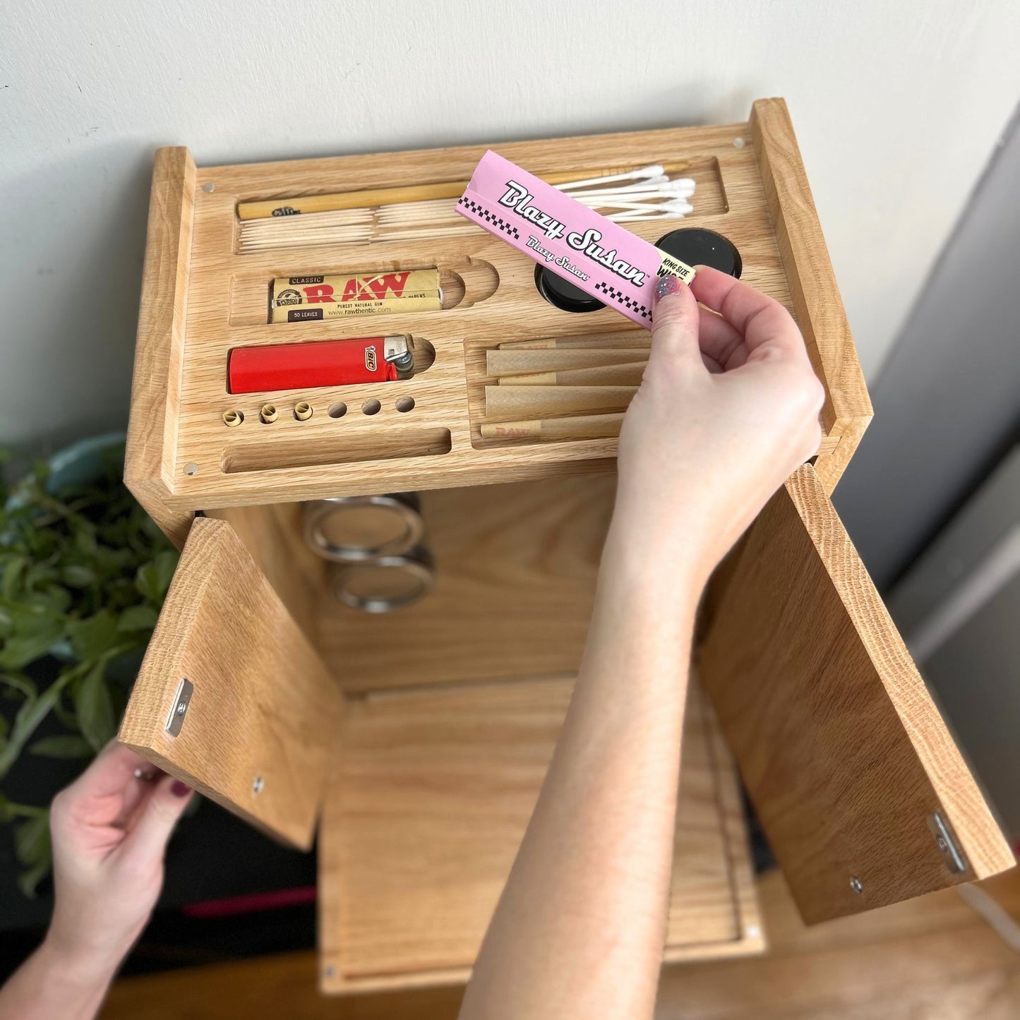 Wooden organizer with compartments, including a rolling papers, being held by a hand.