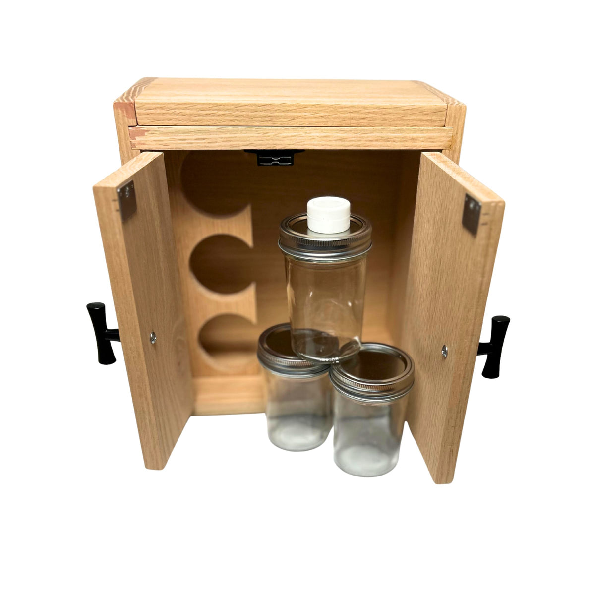 A light natural wood stash box with two doors open, holding three clear mason jars with metal lids and a white concentrate jar. The cabinet has black handles and is shown on a plain white background.